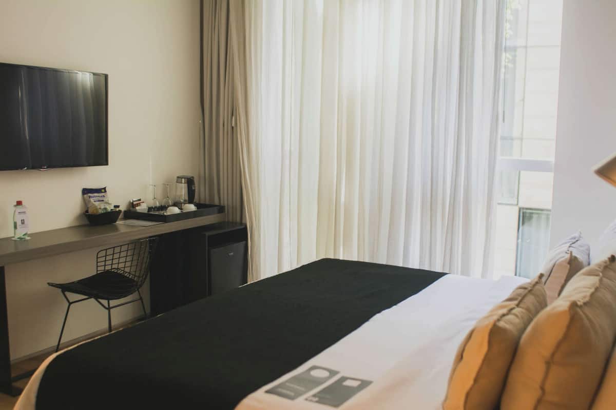 A hotel room with a bed, a desk, a chair, a television, and a window with curtains.
