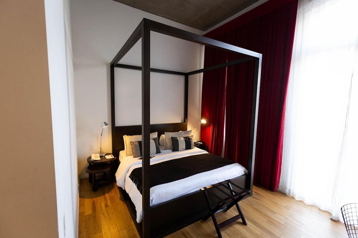 A four-poster bed with a black frame, white bedding, and red curtains.