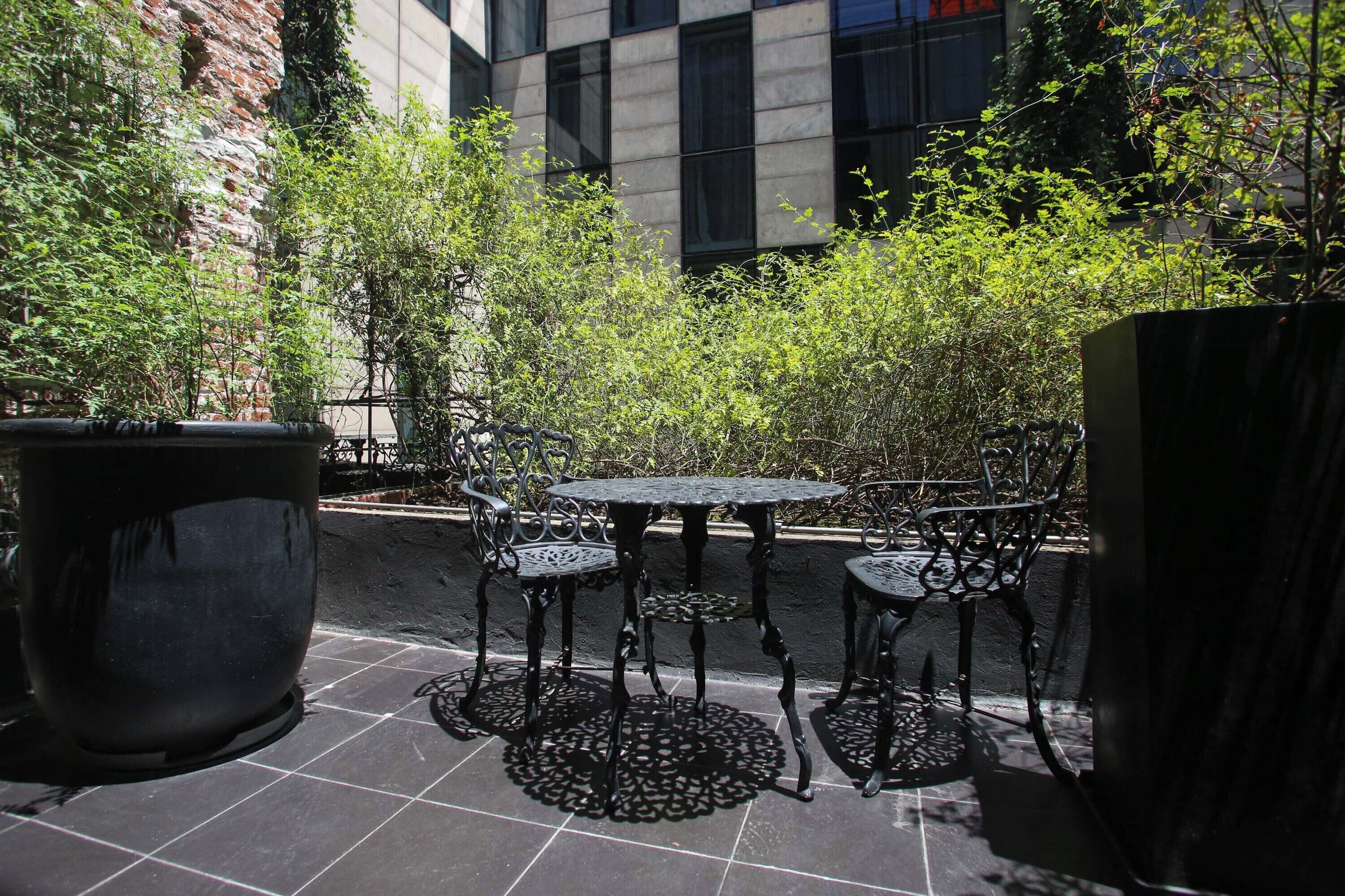 An outdoor patio with a round table and four chairs, surrounded by potted plants and a brick wall.