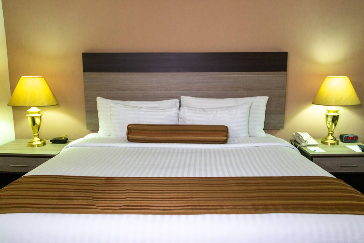 A hotel room with a large bed, two bedside tables, a nightstand, a lamp, and a clock.