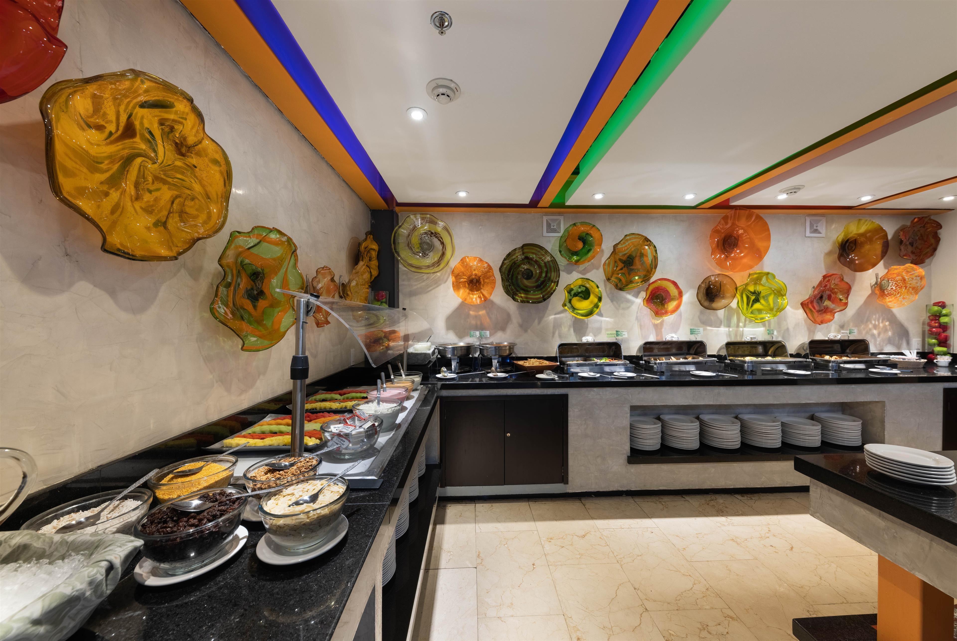 Zona de bufé con diversas opciones de comida y piezas de arte de vidrio decorativas en las paredes.