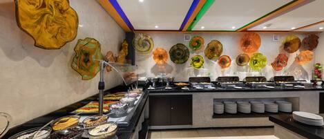 Zona de bufé con diversas opciones de comida y piezas de arte de vidrio decorativas en las paredes.