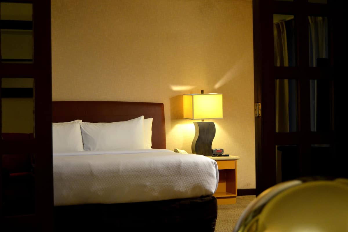 A hotel room with a bed, a bedside lamp, a telephone, and a bookshelf.