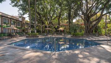 Una piscina con borde de baldosas, rodeada de árboles y mobiliario de exterior.