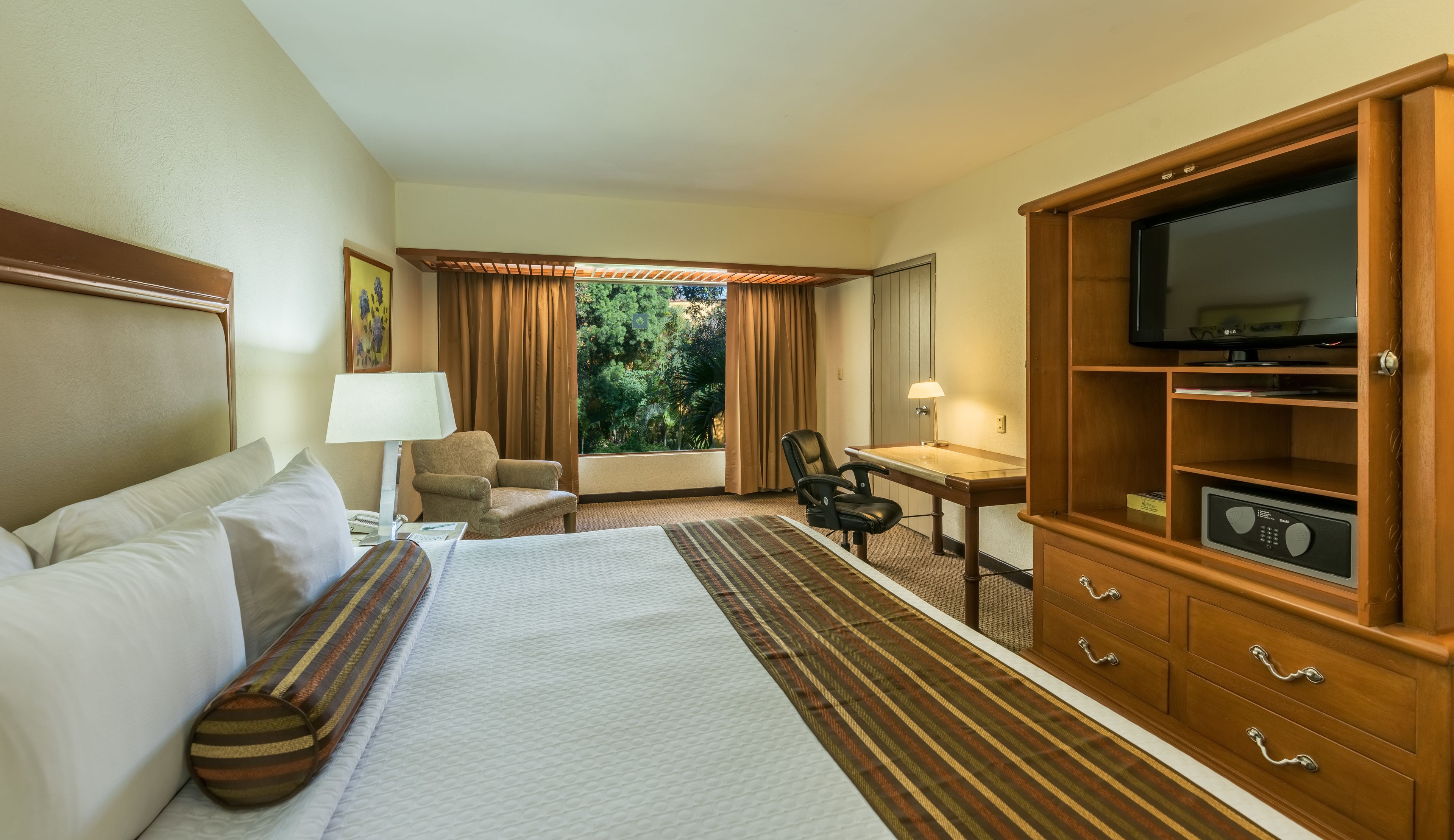 Habitación de hotel con cama, escritorio, silla, televisor y minibar.