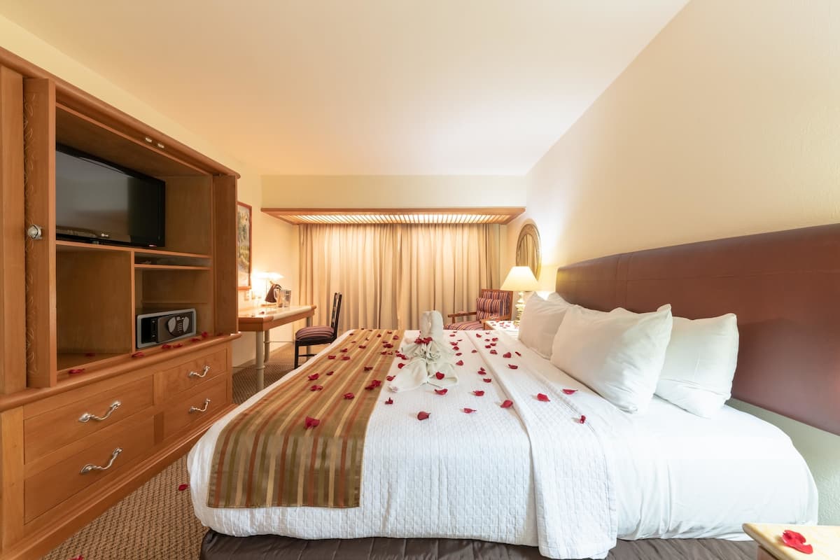 A hotel room with a large bed, a wooden dresser with a TV, a desk, and a chair.
