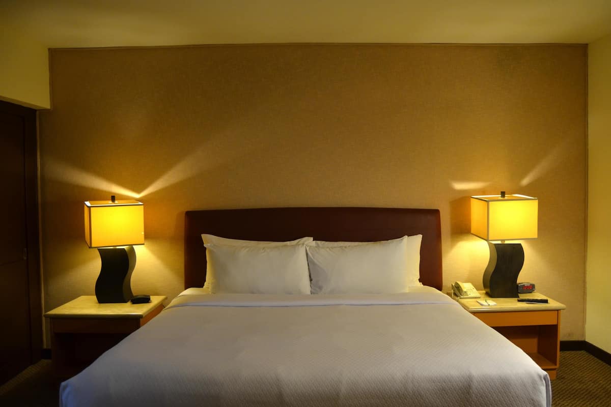 A hotel room with a large bed, two bedside tables with lamps, a nightstand with a phone and clock, and a headboard.