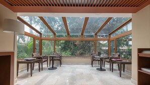 Una habitación iluminada por el sol con techo de vidrio, dos mesas con sillas y una estantería.