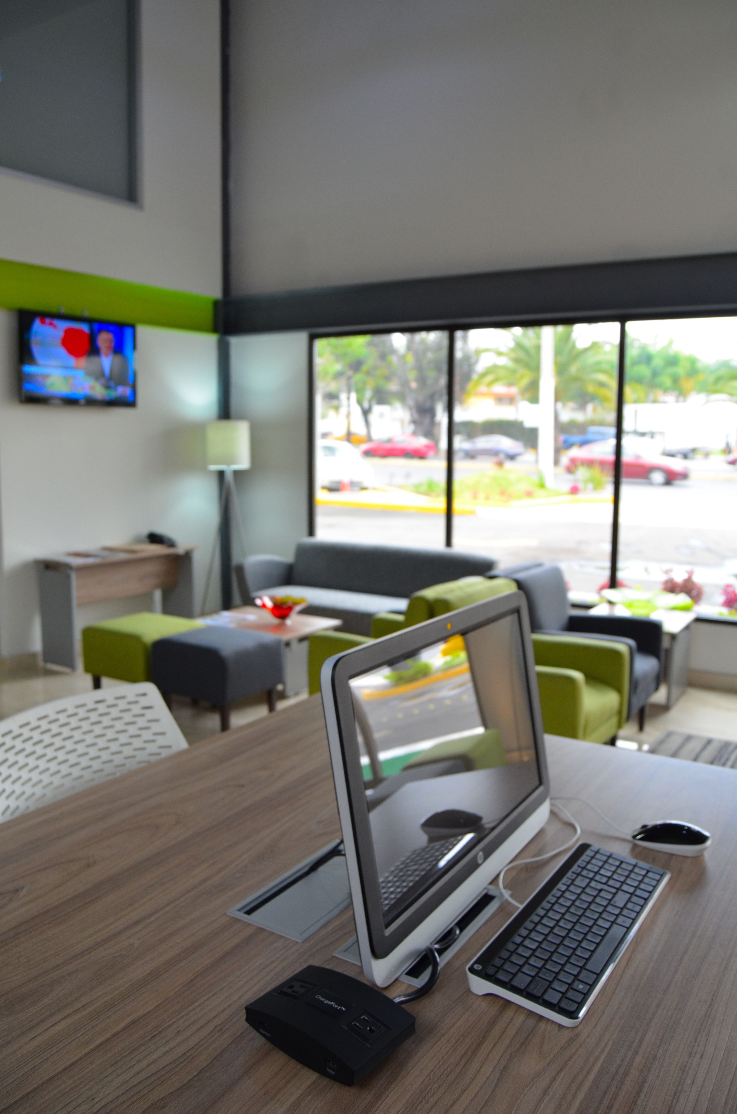 A modern office space with a laptop on a desk, a green couch, and a large window with a view of the street.
