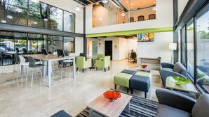 Un moderno vestíbulo de hotel con techo alto, amplias ventanas, zona de comedor y área de descanso con vistas al exterior.