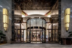 Una entrada imponente con puerta giratoria, paredes de mármol y luminarias modernas.