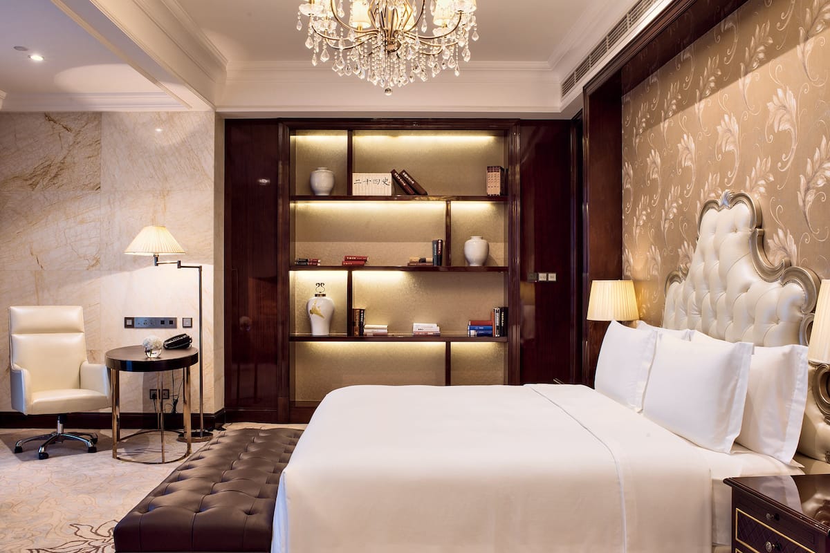 Una habitació d'hotel luxosa amb un llit gran, una butaca còmoda, una petita taula auxiliar, una estanteria i un penjador.