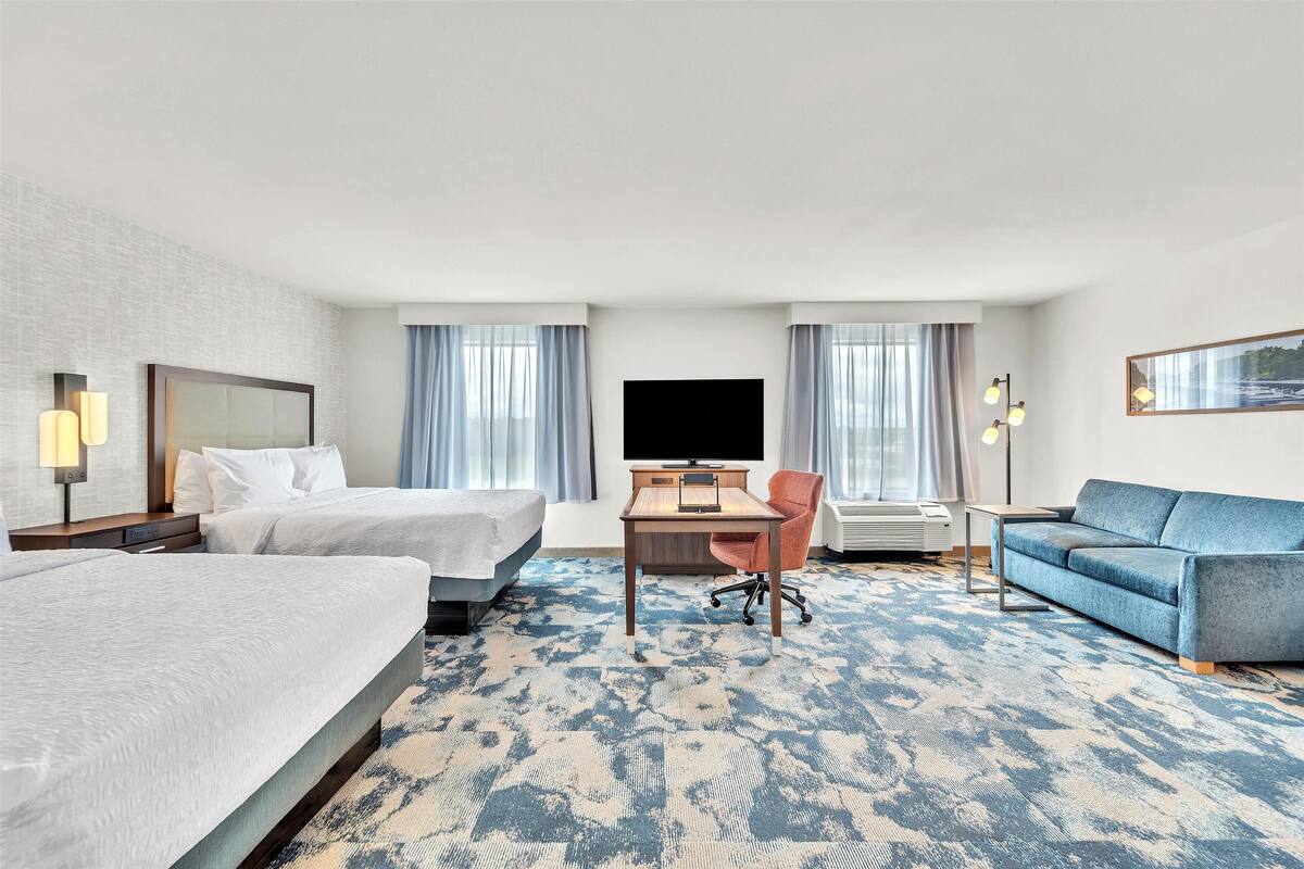 A hotel room with two beds, a desk, a blue sofa, and a TV.