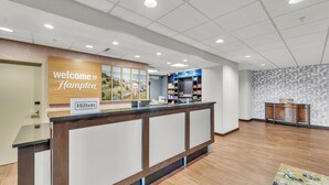 A hotel reception area with a wooden reception desk, a 'Welcome to Hampton' sign, a 'Hilton Honors' sign, and a patterned wall. - Hampton Inn & Suites Kenosha Pleasant Prairie (Kenosha)