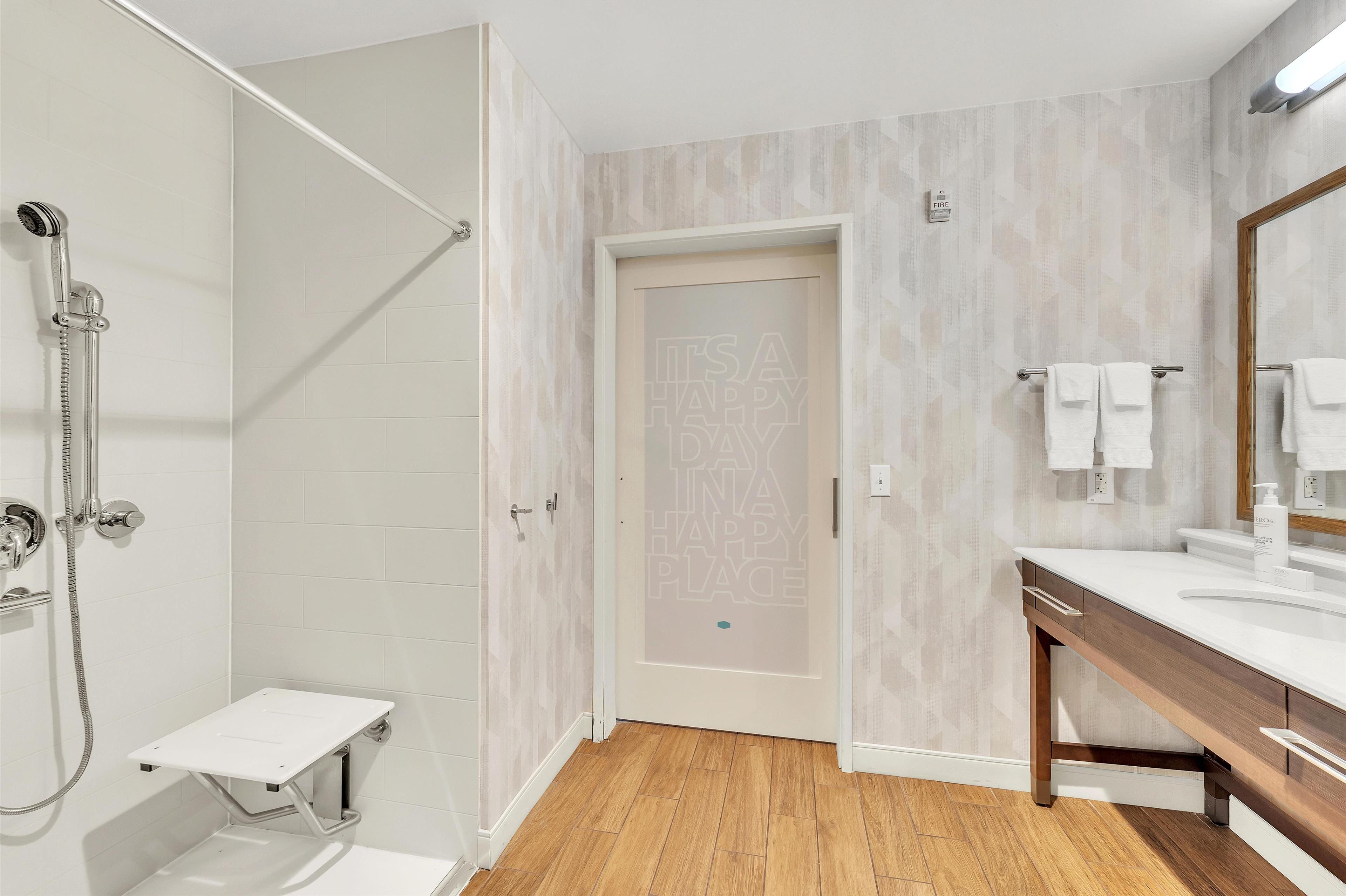 Un baño moderno con ducha, tocador con espejo y puerta con un mensaje motivacional.