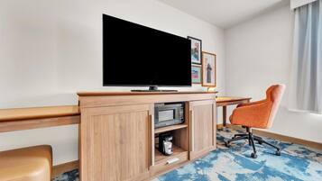 Une chambre d’hôtel équipée d’un téléviseur à écran plat, d’un meuble en bois contenant un four à micro-ondes, d’une machine à café et d’un fauteuil orange.