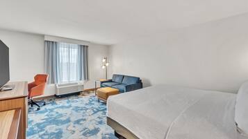 A hotel room with a large bed, a desk, an orange chair, a blue sofa, and a window with curtains.