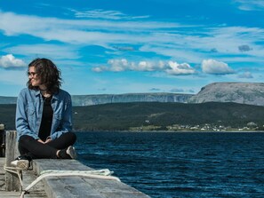 A person sitting on a wooden dock by a body of water with a mountainous landscape in the background. - Marble Inn Resort (Steady Brook)