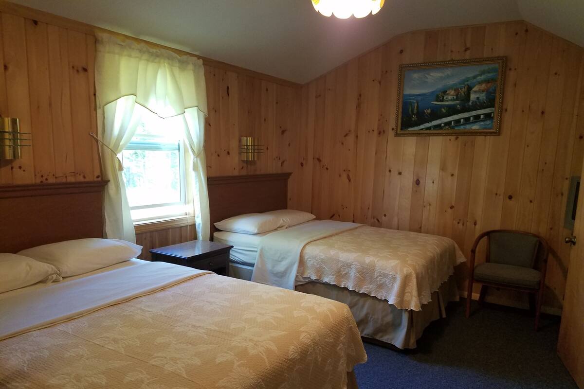 A room with two beds, a chair, a painting on the wall, and a window with curtains.