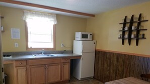 A compact kitchen with a sink, a microwave, and a refrigerator. There is a wooden cabinet and a dining table with chairs. - Sunnyside Motel & Cottages (Bar Harbor)