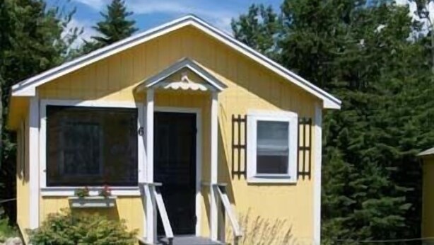 A yellow cabin with a porch, two white chairs, and a small garden. - Sunnyside Motel & Cottages (Bar Harbor)