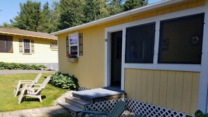 A yellow house with a covered porch, two lawn chairs, and a small step leading to the door. - Sunnyside Motel & Cottages (Bar Harbor)