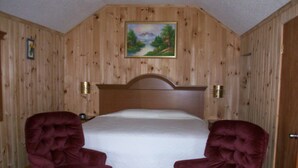 A bedroom with a wooden paneled wall, a bed with a white mattress, and two upholstered chairs. - Sunnyside Motel & Cottages (Bar Harbor)