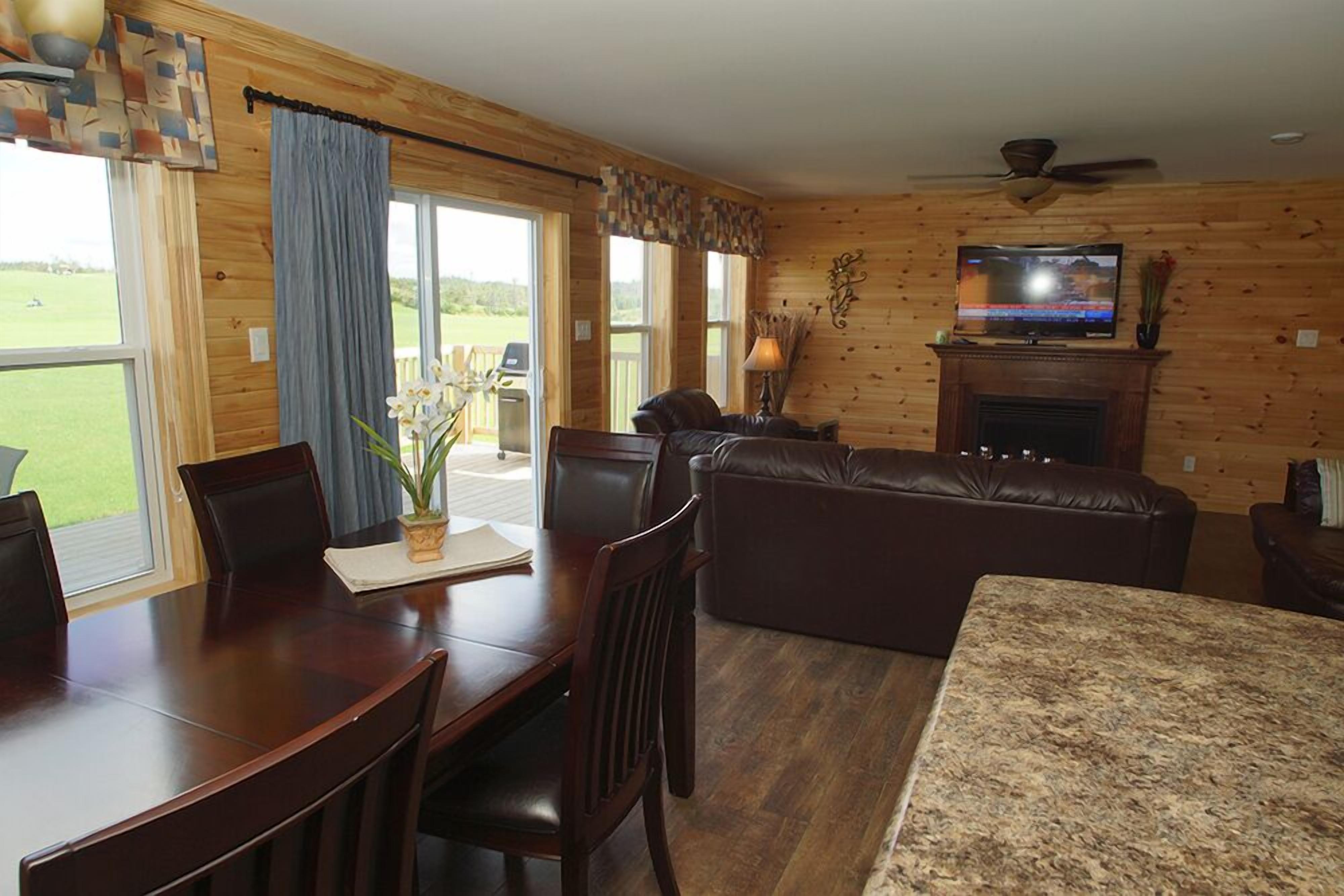 A wooden interior with a dining table, chairs, a sofa, a television, and a fireplace.