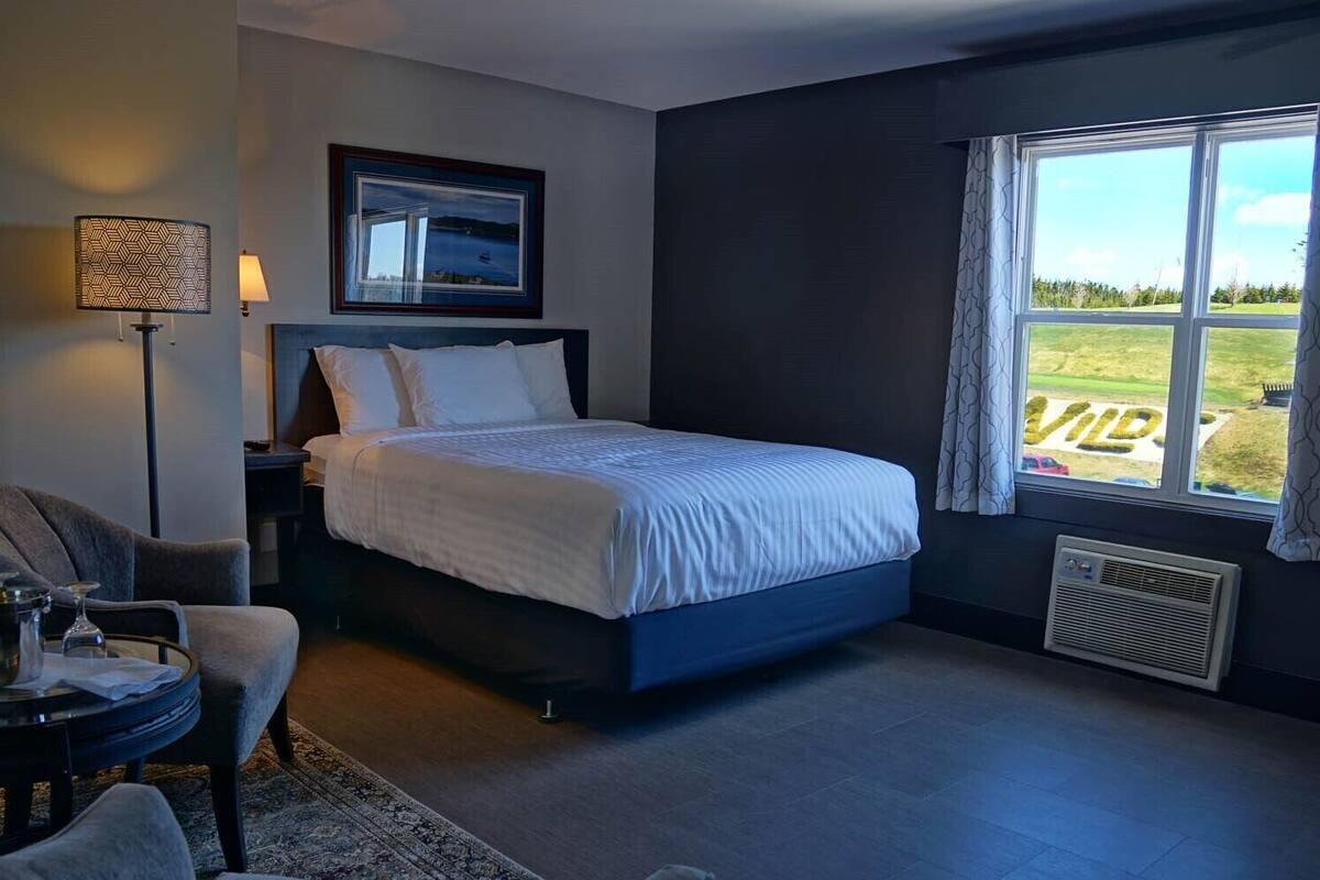 A modern hotel room with a large bed, a desk, a chair, a lamp, and a window with a view of the outdoors.