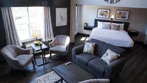Una habitación de hotel moderna con una cama grande, dos sillones, un sofá, una mesita y una lámpara de pie.