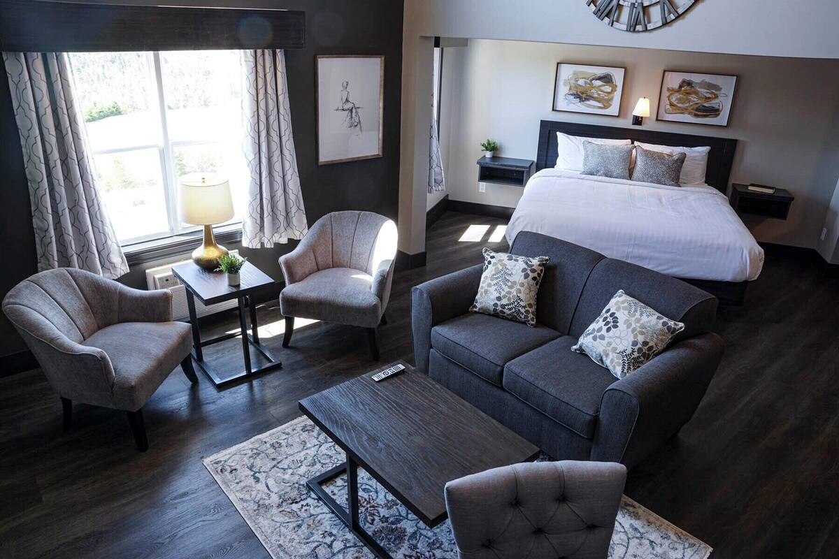 A modern hotel room with a large bed, two armchairs, a sofa, a small table, and a floor lamp.