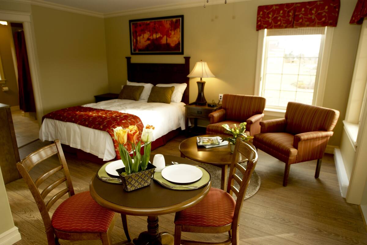 A hotel room with a bed, a dining table with chairs, a lamp, and a window with curtains.