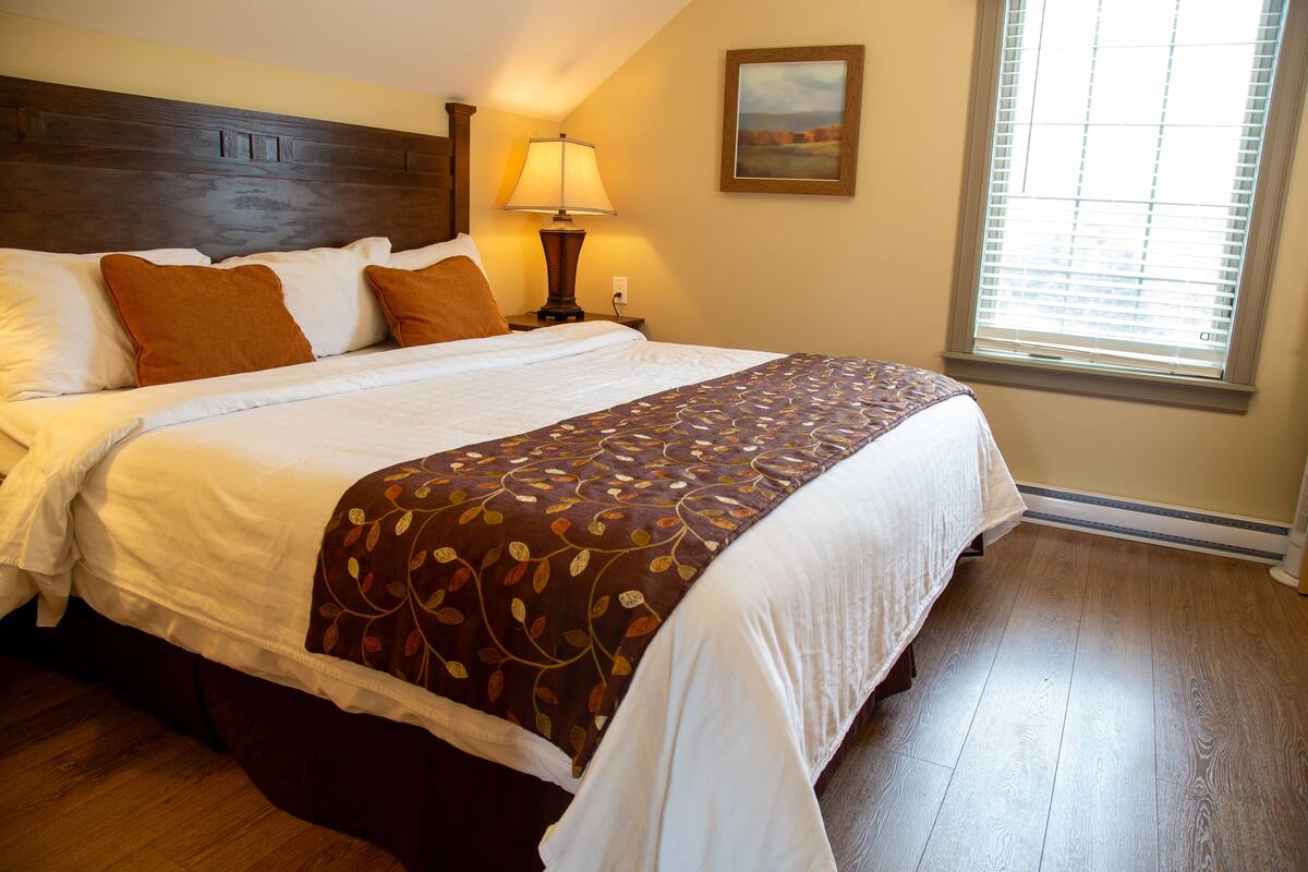 A neatly made bed with a patterned bedspread, a wooden headboard, and a bedside lamp.