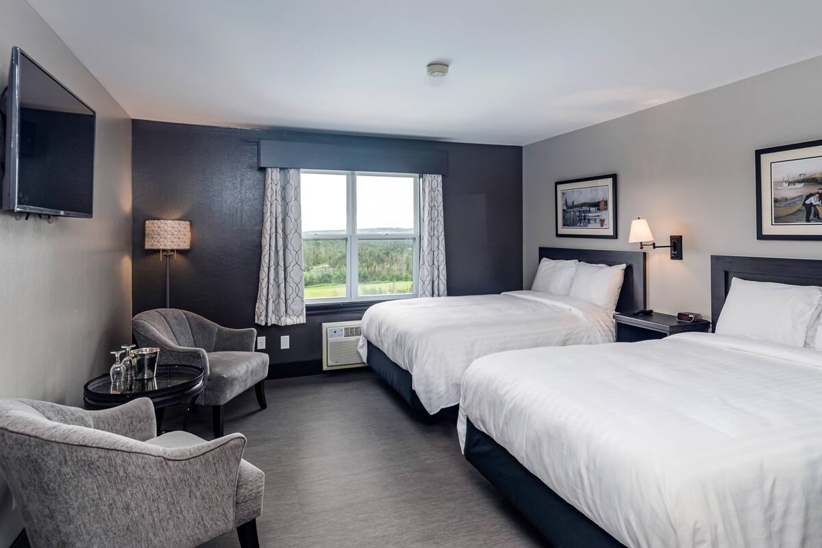 A hotel room with two beds, a desk, a chair, a TV, and a window with a view of the outdoors.