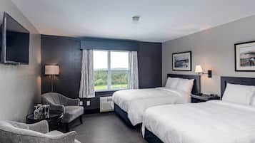 A hotel room with two beds, a desk, a chair, a TV, and a window with a view of the outdoors.