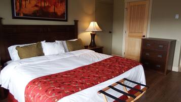 Un lit bien fait, avec une literie blanche et rouge, une tête de lit en bois, une table de chevet avec une lampe, une commode en bois et une porte avec un interrupteur sur le mur.