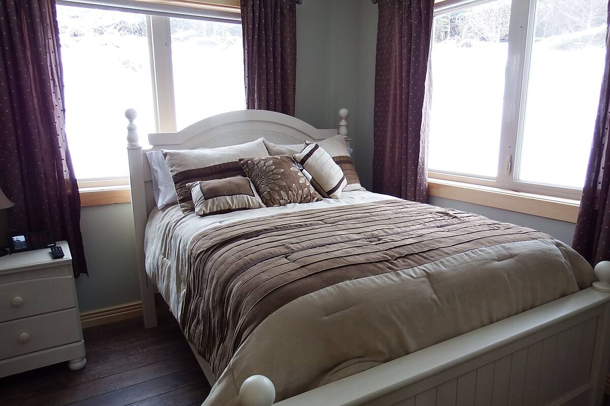 A bedroom with a bed, nightstand, and window with curtains.