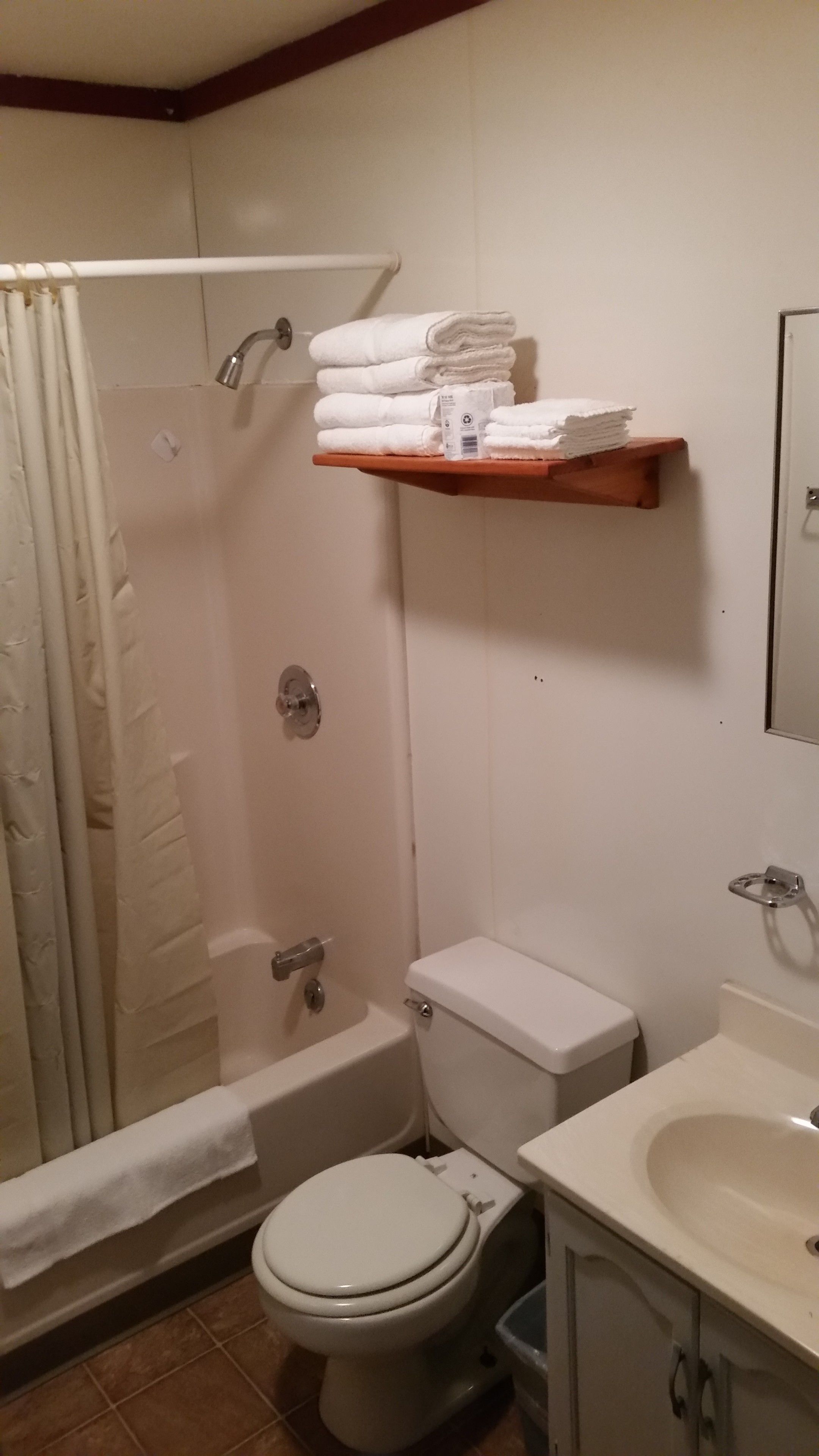 A bathroom with a shower, toilet, and sink. There are towels stacked on a shelf above the toilet.