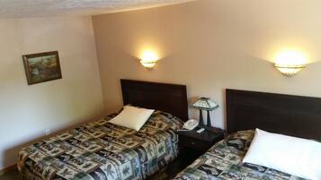 A hotel room with two beds, each with a patterned bedspread and white pillows. There are wall-mounted lamps on either side of the beds.