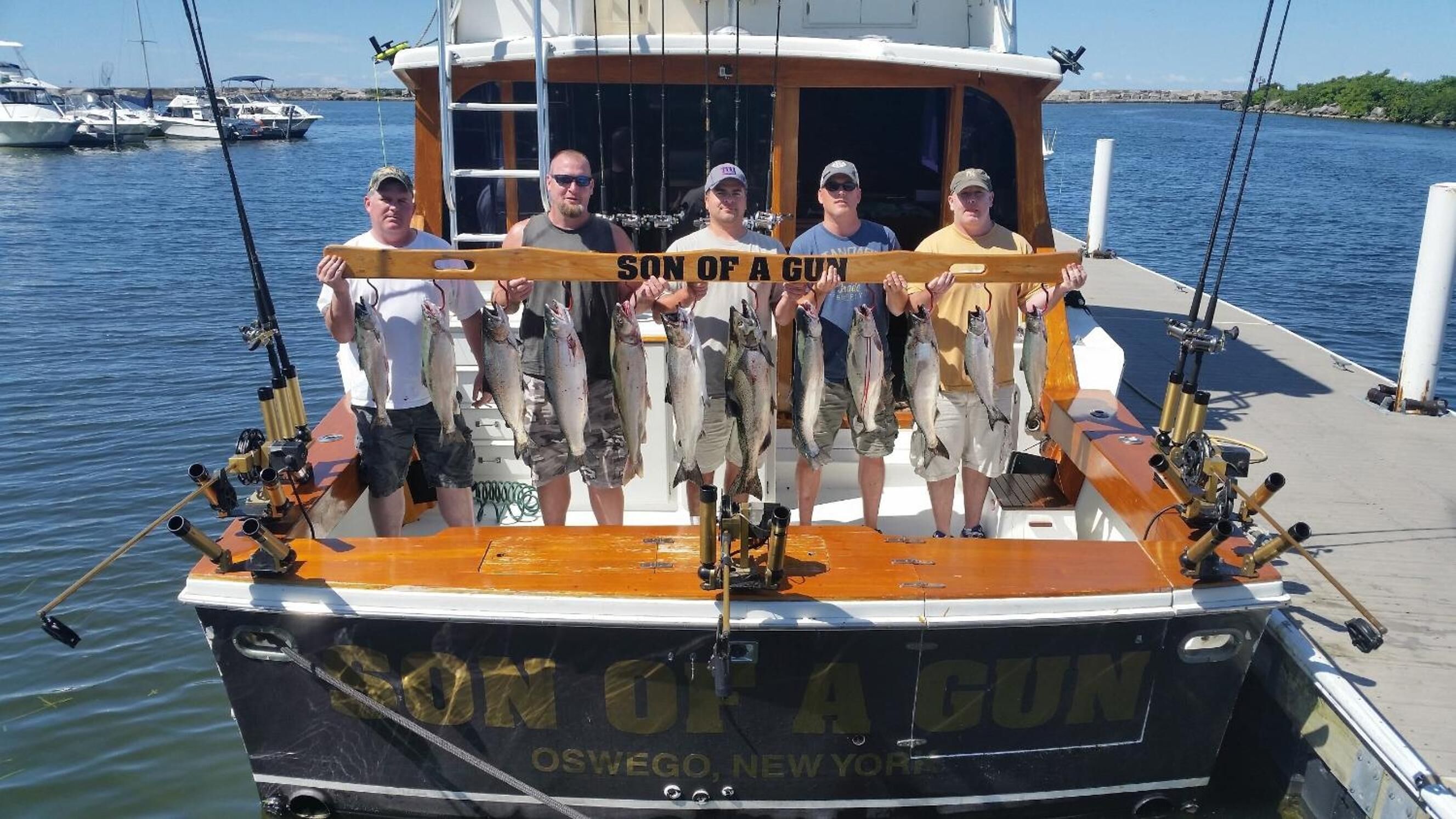 A boat named 'SON OF A GUN' docked at a marina with four people holding fish.