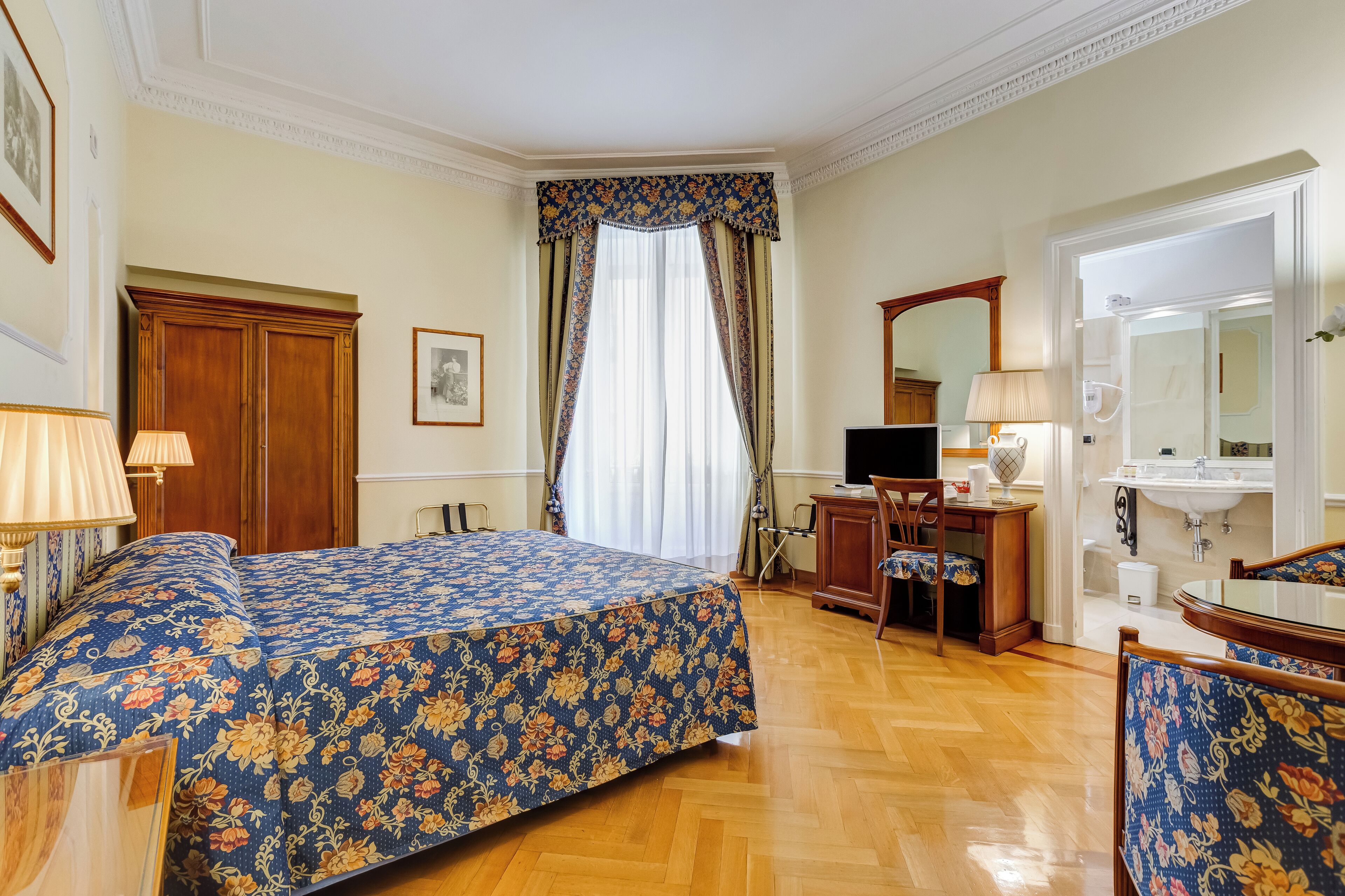 A hotel room with a bed, a desk, a chair, a television, a mirror, and a bathroom.