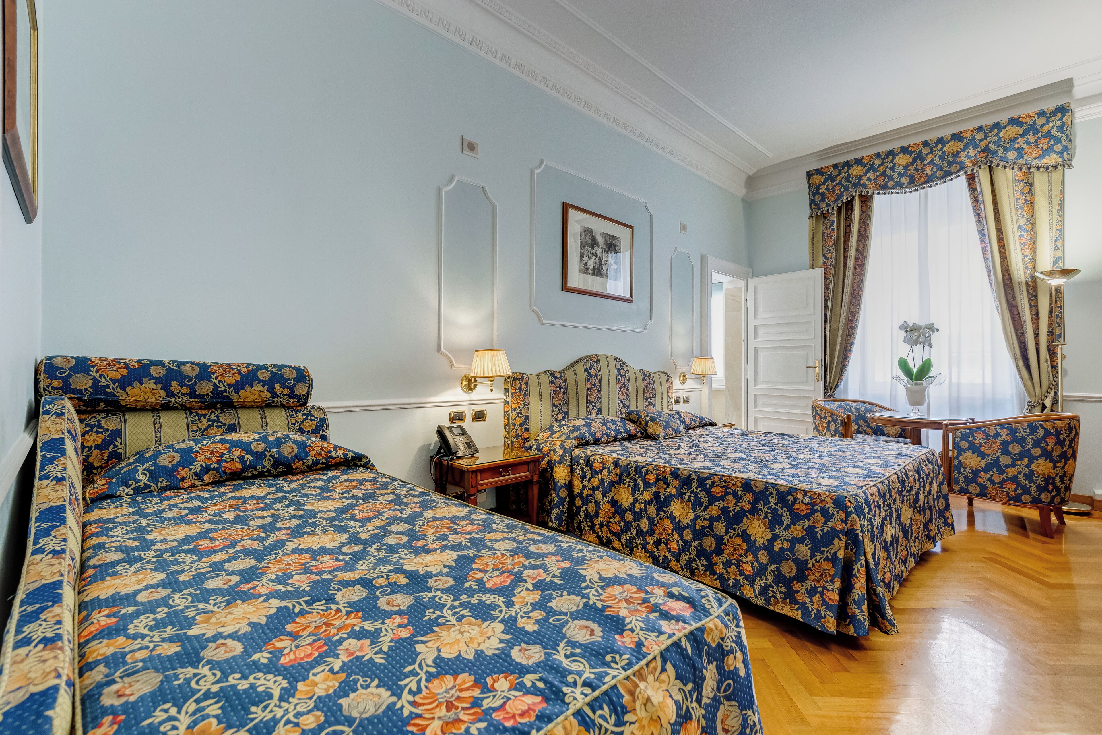 Una habitación de hotel con dos camas, una zona de estar y un ventanal con cortinas.