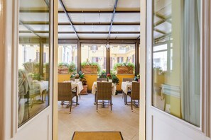 An indoor patio area with wicker furniture, yellow walls, and potted plants. - Hotel Cellini (Rome)
