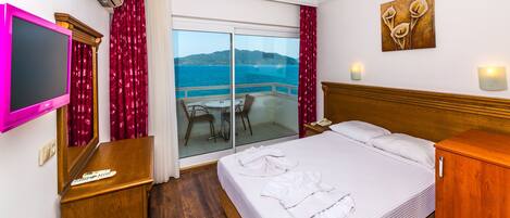 A hotel room with a bed, a TV, a desk, a phone, and a view of the sea.