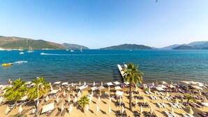 A beach with rows of sun loungers and umbrellas, a clear blue sky, and boats in the water. - Honeymoon Hotel (Marmaris)