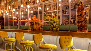 A bar area with yellow bar stools, a display of bottles, and a basket of oranges. - Honeymoon Hotel (Marmaris)