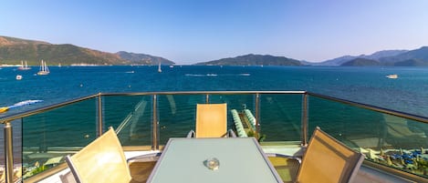 A deck with a table and chairs overlooking a body of water with boats and distant hills.