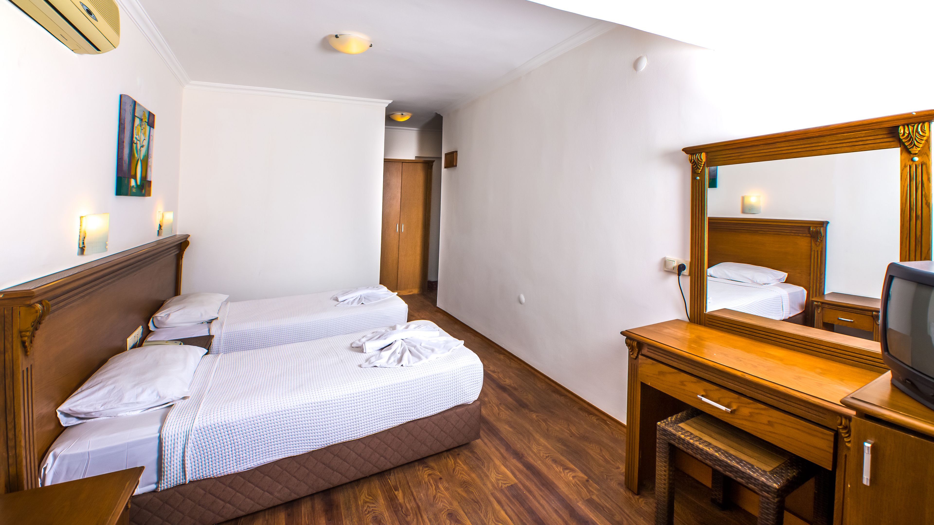 Habitación de hotel con dos camas, un aparador de madera, un televisor y un espejo.