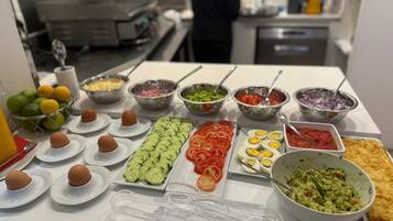Una mesa de buffet con diversos alimentos, incluyendo huevos, pepinos, tomates y un plato de guacamole.