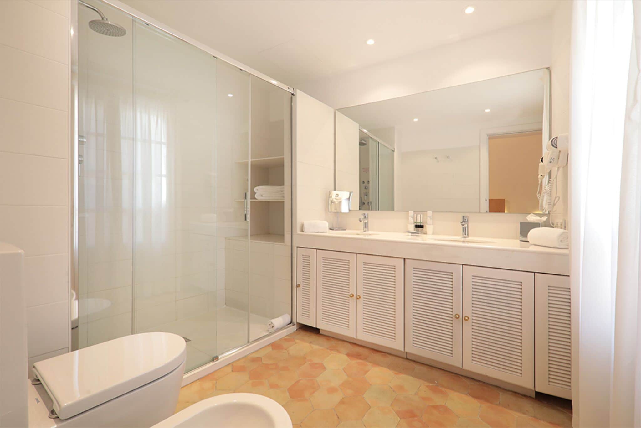 Un baño moderno con ducha envuelta en vidrio, inodoro blanco y tocador con un espejo grande.